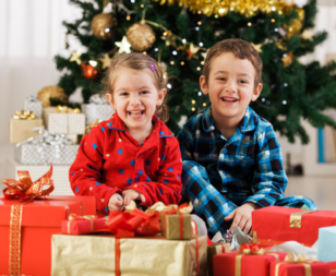 two kids with presents by the christmas tree