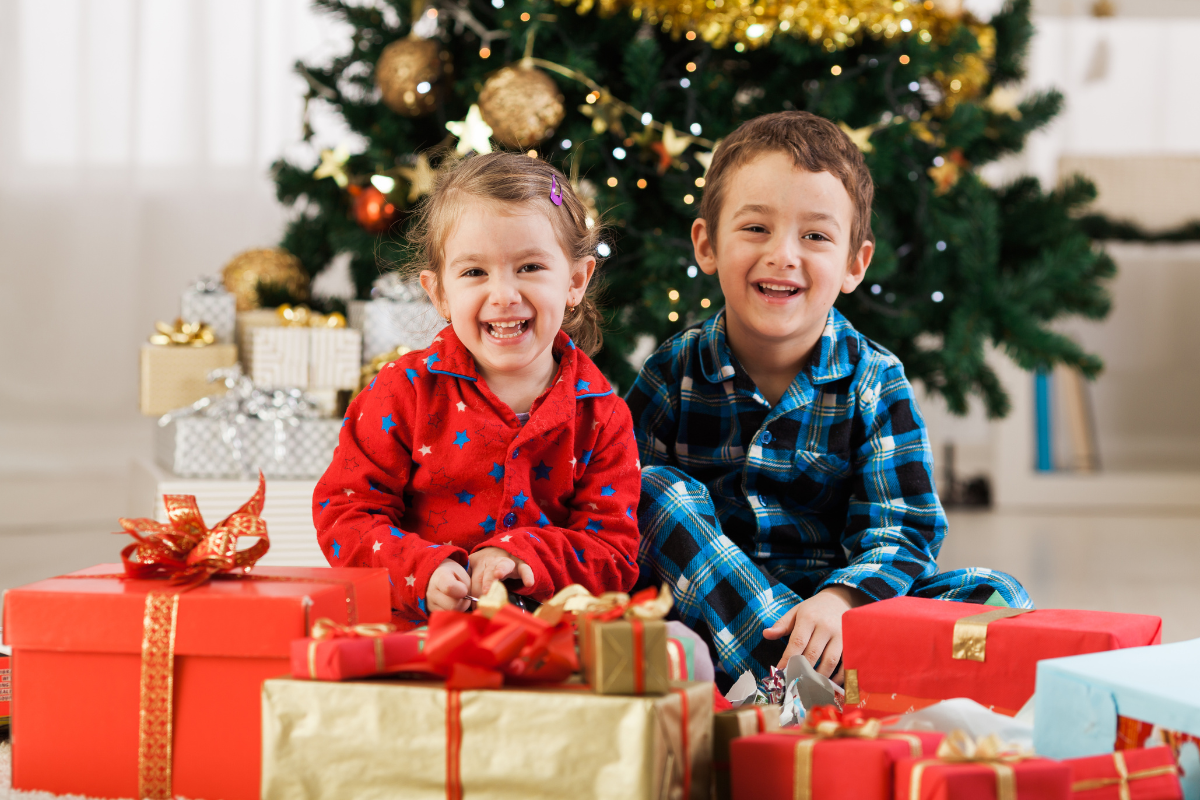 two kids with presents by the christmas tree