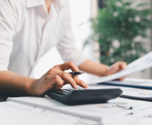 person at a desk with papers typing into a calculator
