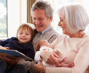 two grandparents holding a baby and a toddler reading a book