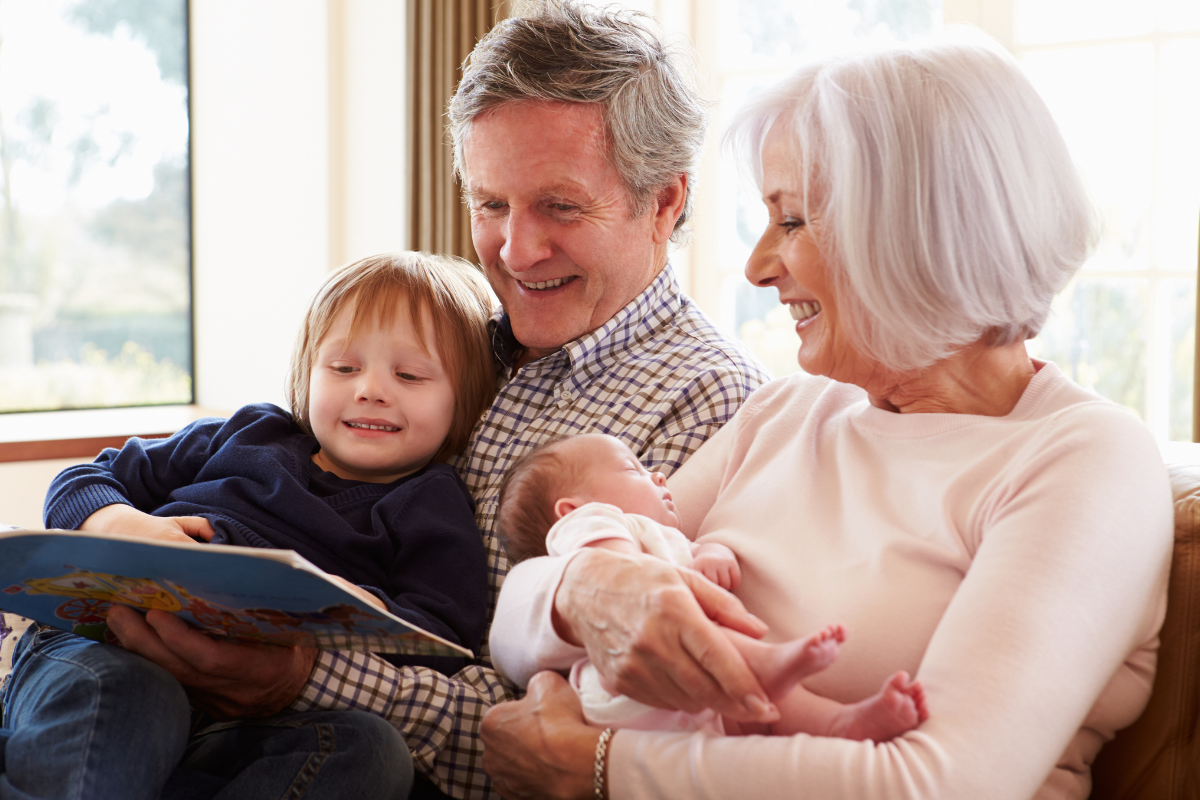 two grandparents holding a baby and a toddler reading a book