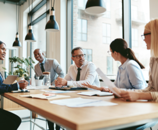 group of business people sitting around a table with papers talking