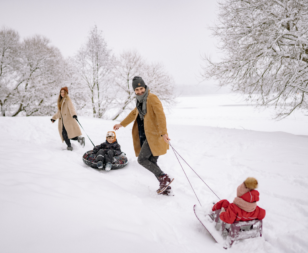 mom, dad, and 2 kids playing on sleds in the winter
