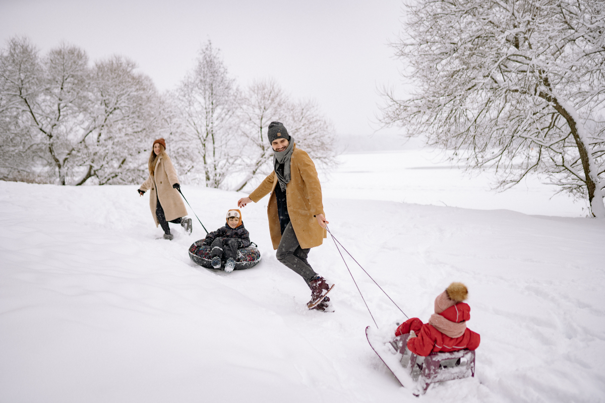 mom, dad, and 2 kids playing on sleds in the winter
