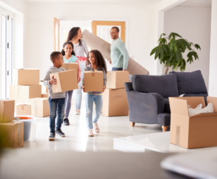 to parents and three kids holding moving boxes with more boxes in the room