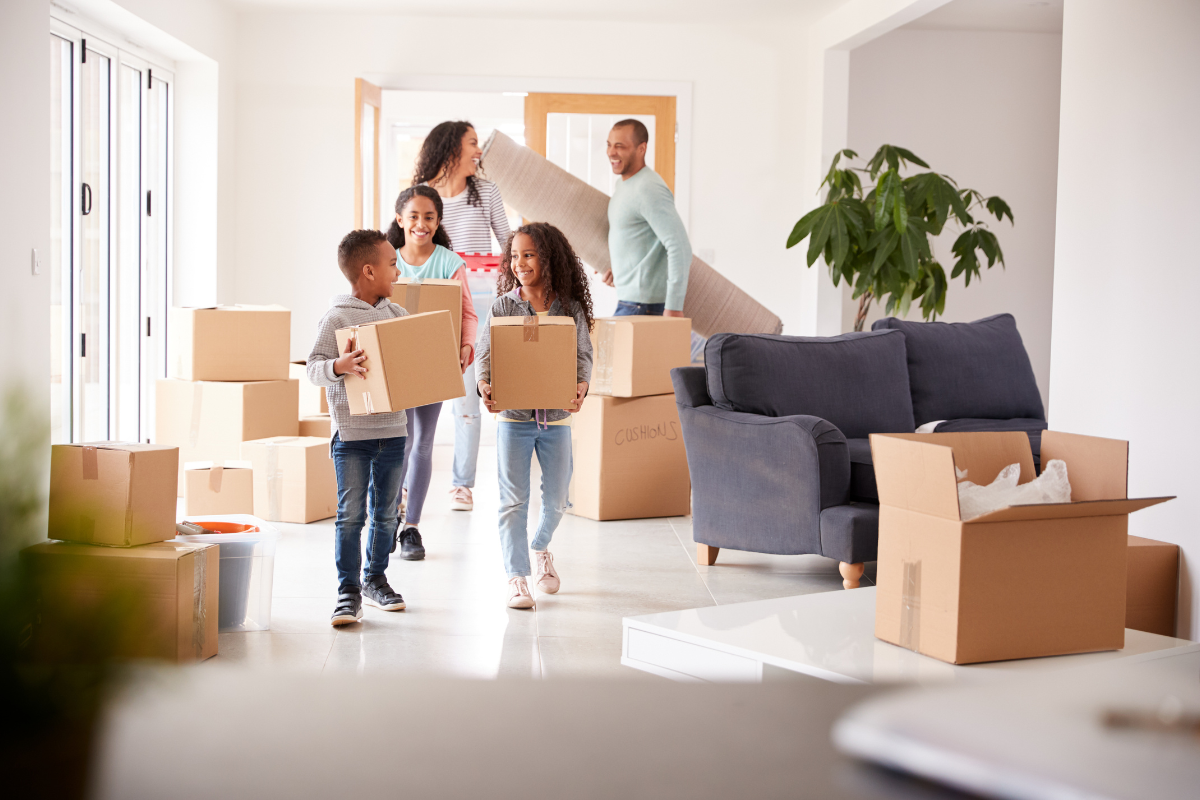 to parents and three kids holding moving boxes with more boxes in the room