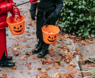 2 kids dressed up in black and red halloween costumes carrying jack o lantern trick-or-treating buckets